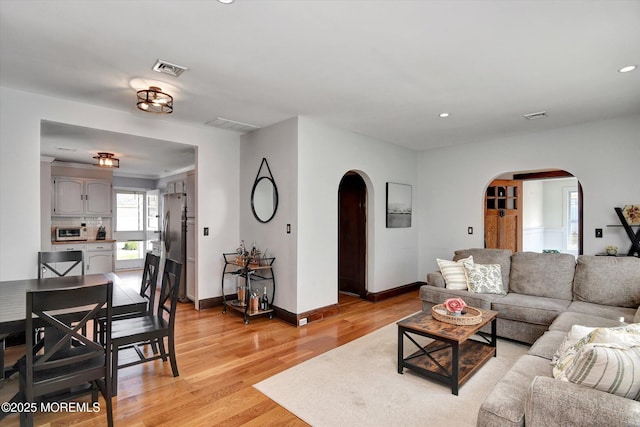 living area with recessed lighting, arched walkways, light wood-style flooring, and baseboards