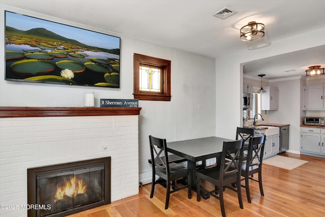 dining room with baseboards, visible vents, a fireplace, and light wood-style flooring