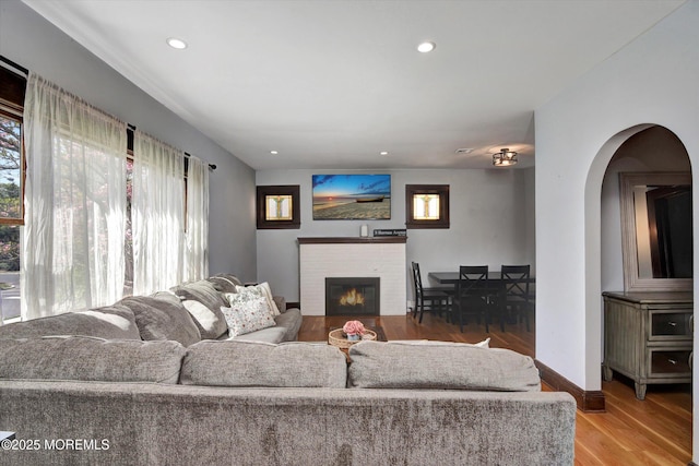 living area featuring light wood-style floors, arched walkways, baseboards, recessed lighting, and a fireplace