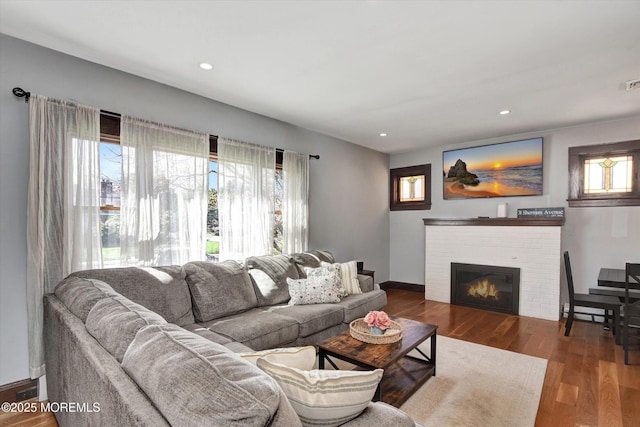 living area with visible vents, baseboards, recessed lighting, a brick fireplace, and wood finished floors