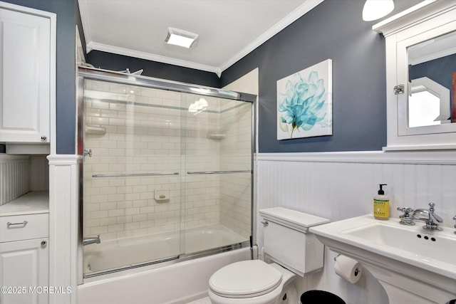 bathroom with a sink, toilet, enclosed tub / shower combo, ornamental molding, and wainscoting