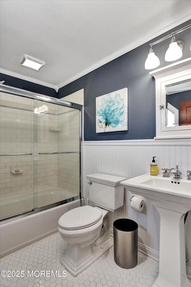 bathroom featuring crown molding, shower / bath combination with glass door, toilet, tile patterned floors, and wainscoting