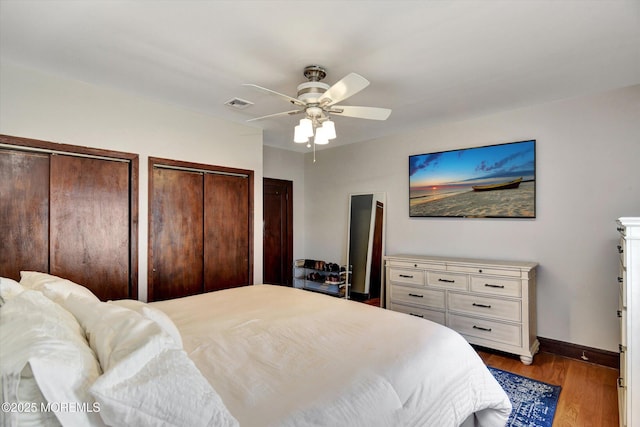 bedroom with visible vents, baseboards, wood finished floors, multiple closets, and a ceiling fan