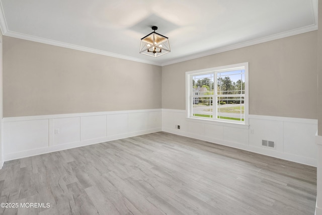 empty room featuring visible vents, crown molding, wood finished floors, a wainscoted wall, and an inviting chandelier