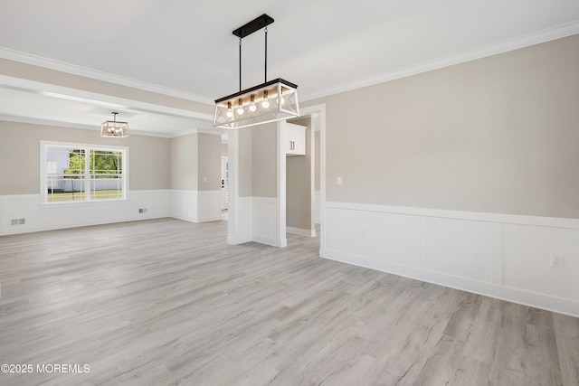 spare room featuring an inviting chandelier, light wood-style floors, crown molding, and wainscoting