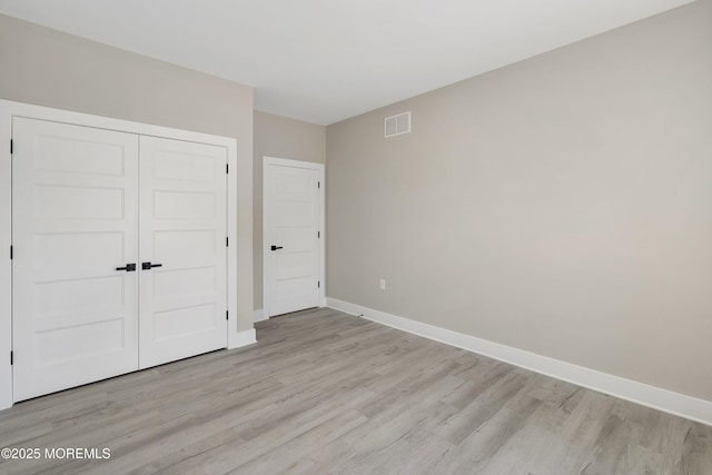unfurnished bedroom featuring visible vents, light wood-style floors, baseboards, and a closet