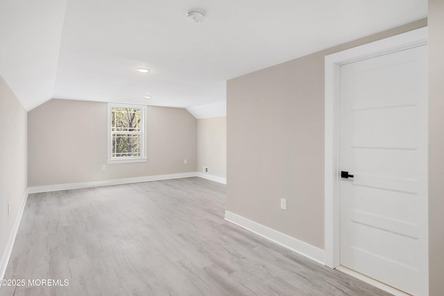 additional living space with baseboards, light wood finished floors, and vaulted ceiling