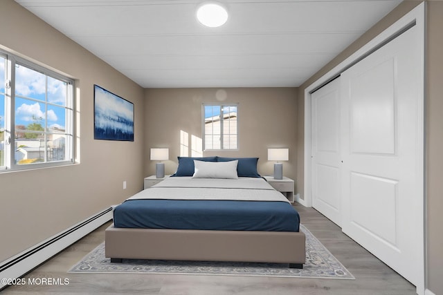 bedroom with a closet, light wood finished floors, and a baseboard heating unit