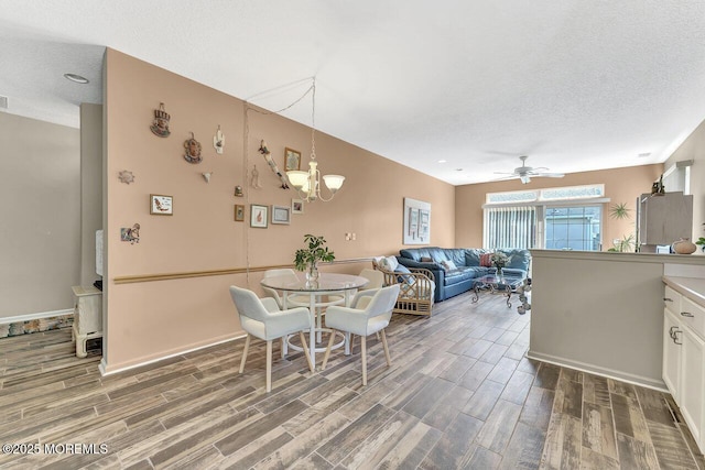 dining space with baseboards, a textured ceiling, ceiling fan with notable chandelier, and wood finished floors