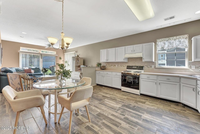 kitchen featuring white cabinets, a notable chandelier, under cabinet range hood, visible vents, and range with gas cooktop
