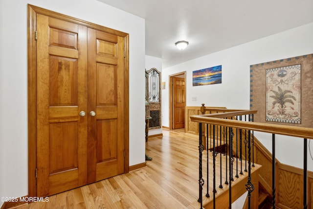 hallway with baseboards, an upstairs landing, and light wood-type flooring