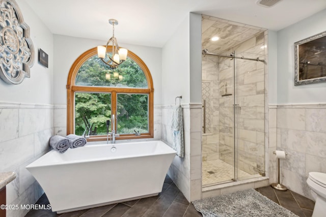bathroom featuring wainscoting, toilet, a freestanding tub, tile walls, and a stall shower