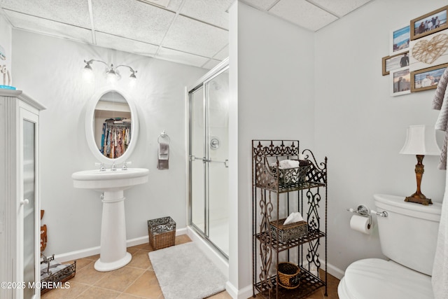 full bathroom with toilet, a drop ceiling, tile patterned flooring, and a stall shower