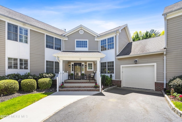 view of front facade with an attached garage, a shingled roof, driveway, and covered porch