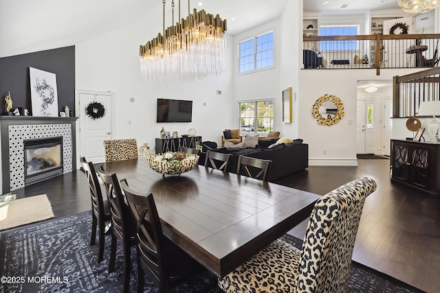 dining area featuring a high ceiling, an inviting chandelier, a fireplace, baseboards, and wood finished floors