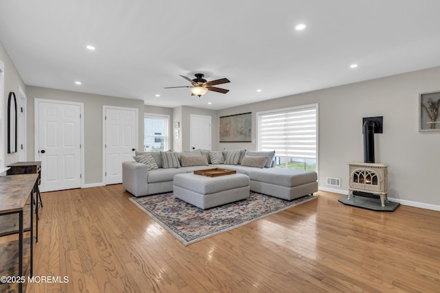 living room with wood finished floors, ceiling fan, baseboards, visible vents, and a wood stove