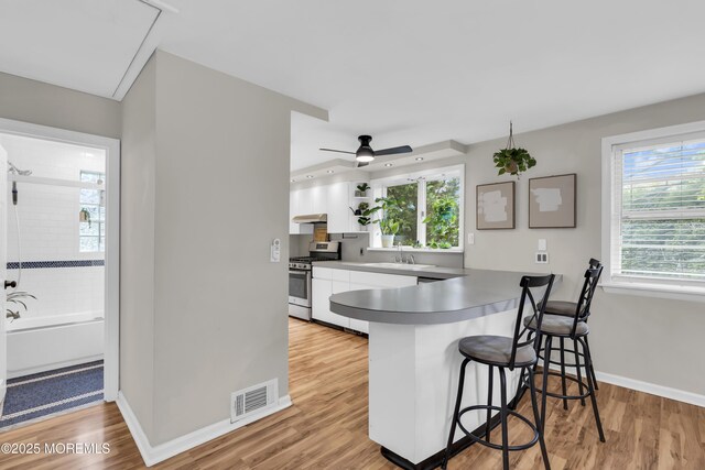 kitchen with gas range, white cabinets, a sink, visible vents, and a peninsula