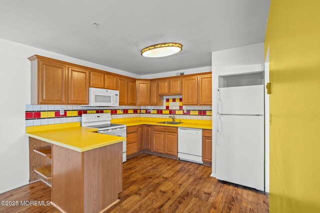 kitchen with a sink, white appliances, a peninsula, wood finished floors, and tasteful backsplash