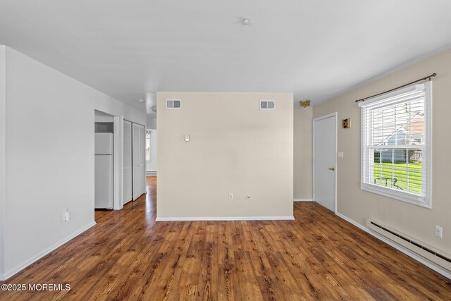 spare room featuring baseboards, baseboard heating, wood finished floors, and visible vents