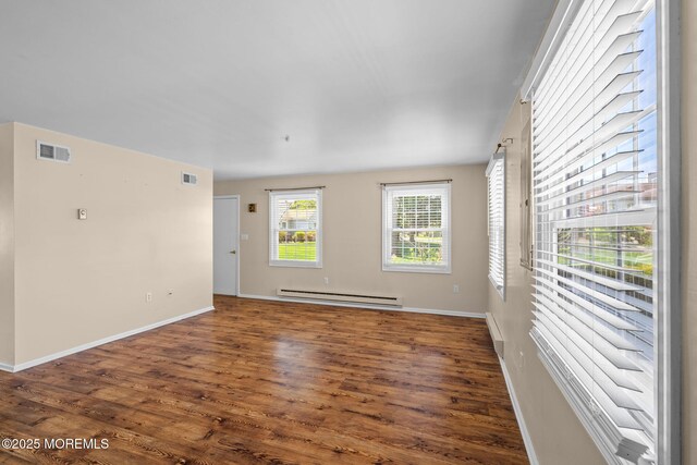 unfurnished room featuring baseboards, visible vents, baseboard heating, and wood finished floors