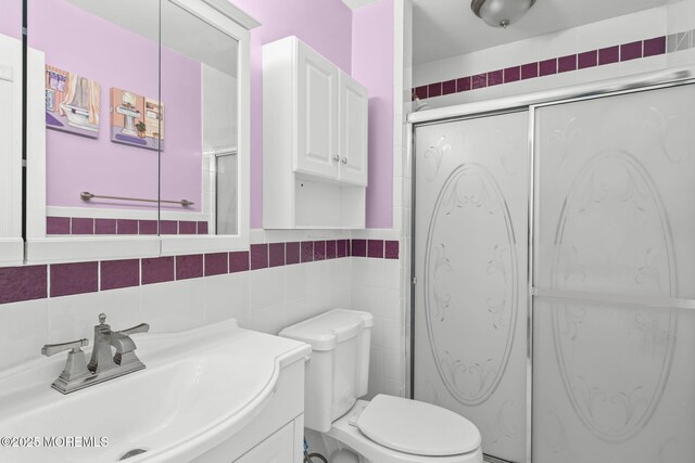 full bathroom featuring toilet, a shower with door, tile walls, and vanity