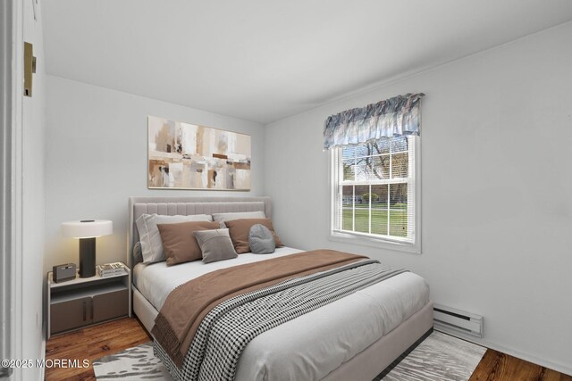 bedroom with wood finished floors and a baseboard heating unit