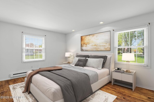 bedroom with multiple windows, wood finished floors, and a baseboard radiator