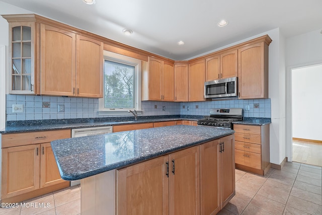 kitchen featuring appliances with stainless steel finishes, a center island, a sink, glass insert cabinets, and dark stone counters