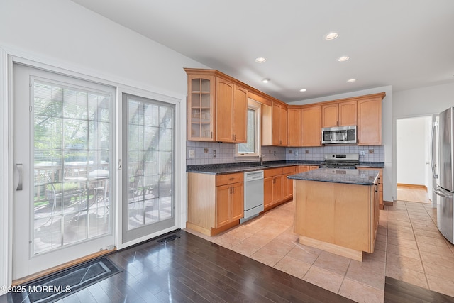 kitchen with backsplash, a center island, dark stone countertops, glass insert cabinets, and stainless steel appliances