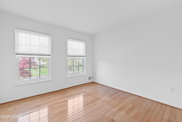 spare room with baseboards, wood finished floors, and visible vents