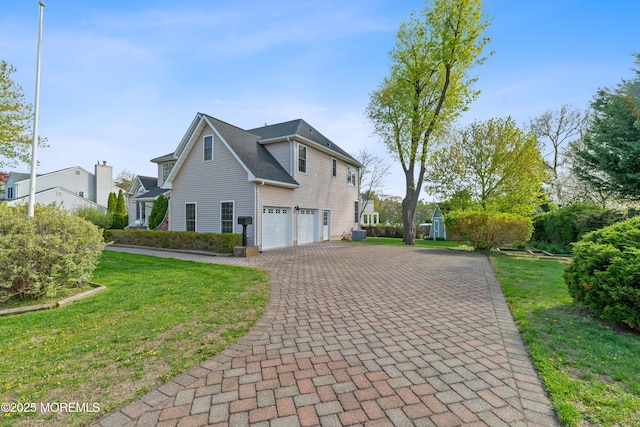 view of side of home with an attached garage, a yard, and decorative driveway