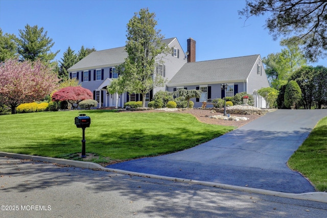 view of front of property with a chimney, driveway, and a front lawn