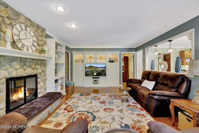 living area with ornamental molding, light wood-type flooring, a stone fireplace, and recessed lighting