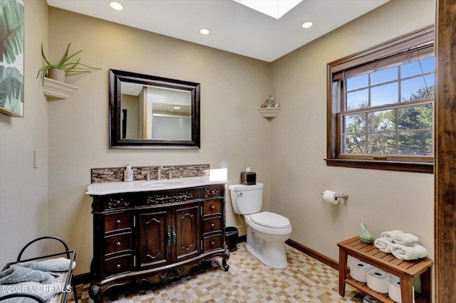 bathroom featuring a skylight, baseboards, toilet, recessed lighting, and vanity