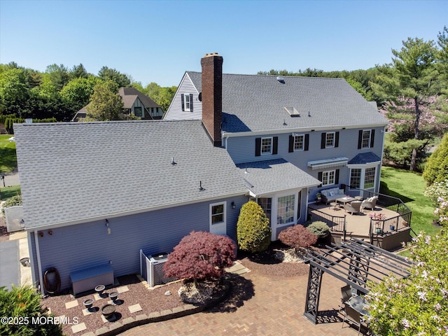 back of house with a wooden deck, a chimney, a shingled roof, central air condition unit, and outdoor dining space