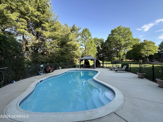 view of pool with a gazebo, fence, a patio area, and view of scattered trees