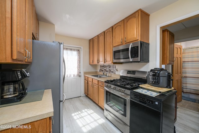kitchen with a sink, appliances with stainless steel finishes, brown cabinets, and light countertops