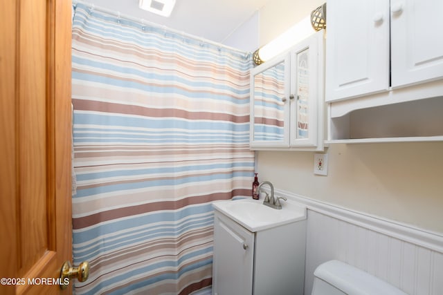 full bath with toilet, a shower with curtain, a wainscoted wall, and vanity