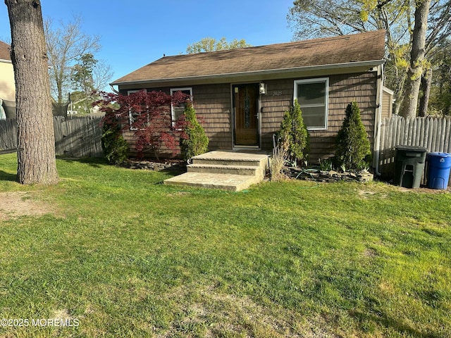 bungalow-style house featuring a shingled roof, a front lawn, and fence