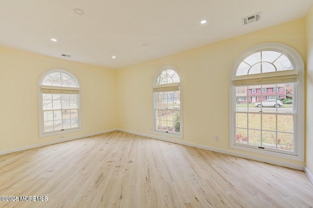 empty room with baseboards, visible vents, plenty of natural light, and wood finished floors
