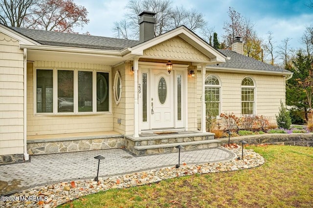 doorway to property with roof with shingles, a chimney, and a lawn