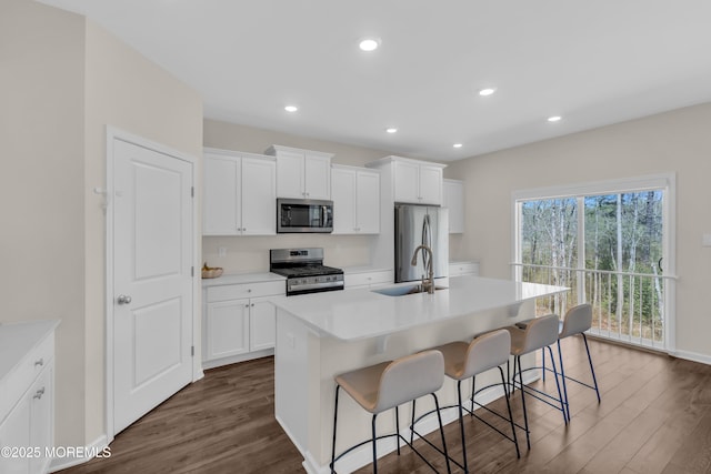 kitchen featuring a center island with sink, a kitchen breakfast bar, stainless steel appliances, and dark wood-style flooring