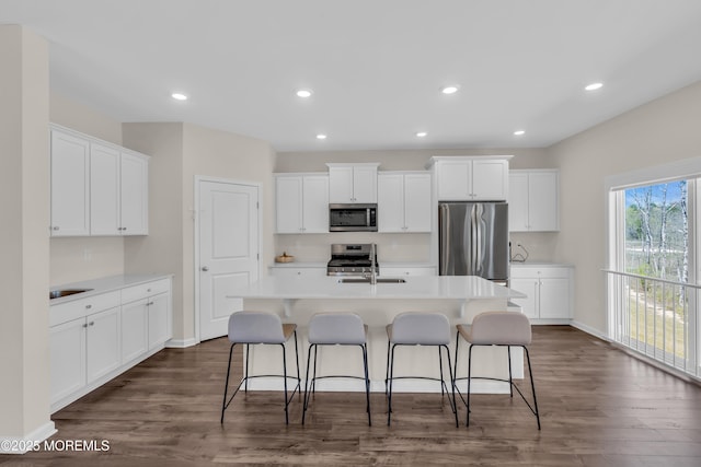 kitchen with appliances with stainless steel finishes, dark wood finished floors, a sink, white cabinetry, and an island with sink