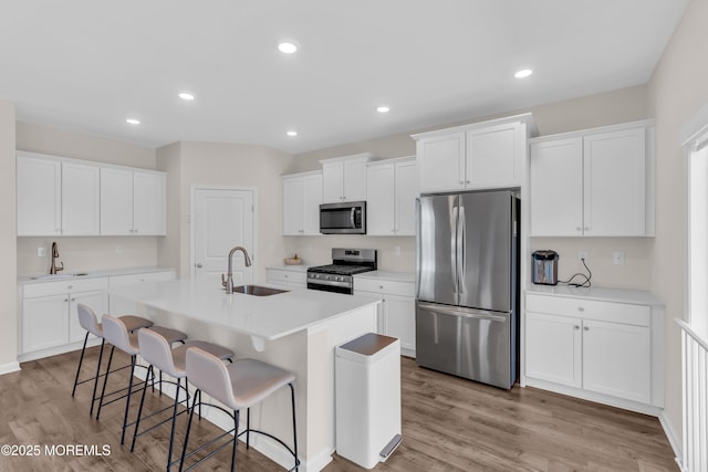 kitchen with a sink, appliances with stainless steel finishes, a center island with sink, and light wood-type flooring