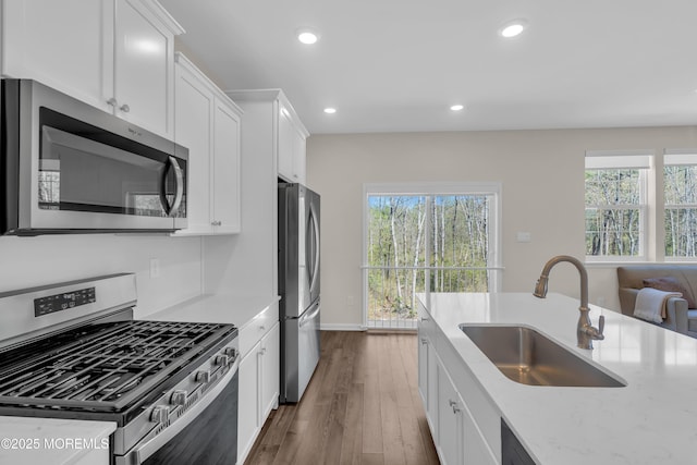kitchen featuring wood finished floors, light stone countertops, white cabinetry, a sink, and appliances with stainless steel finishes