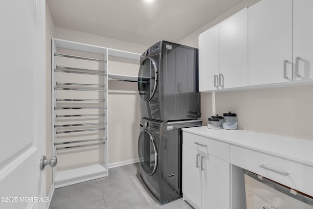 clothes washing area featuring stacked washing maching and dryer, light tile patterned floors, and cabinet space