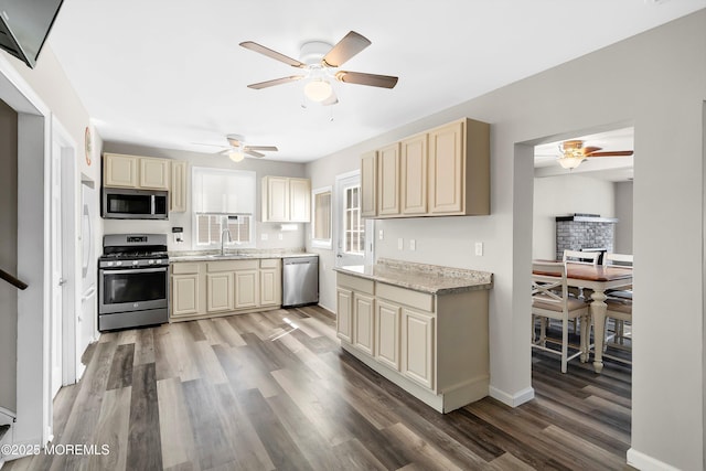 kitchen with wood finished floors, ceiling fan, cream cabinetry, a sink, and stainless steel appliances
