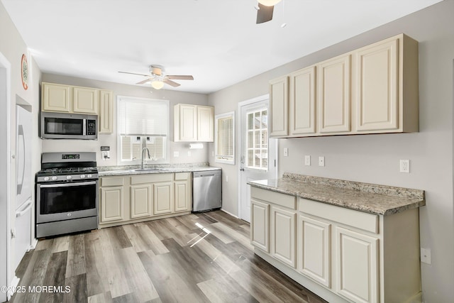 kitchen featuring ceiling fan, light wood-type flooring, a sink, stainless steel appliances, and cream cabinetry