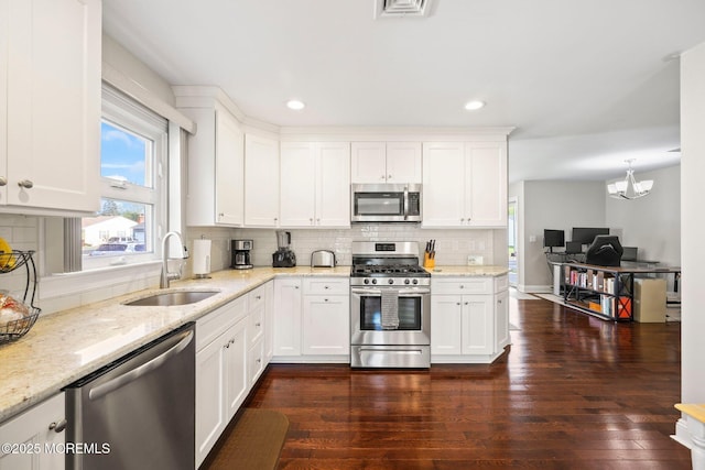 kitchen with appliances with stainless steel finishes, a sink, dark wood finished floors, white cabinetry, and decorative backsplash