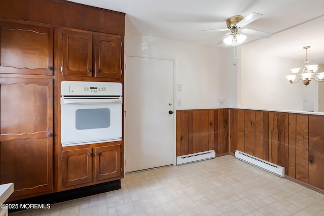 kitchen with wainscoting, baseboard heating, white oven, a baseboard heating unit, and ceiling fan with notable chandelier